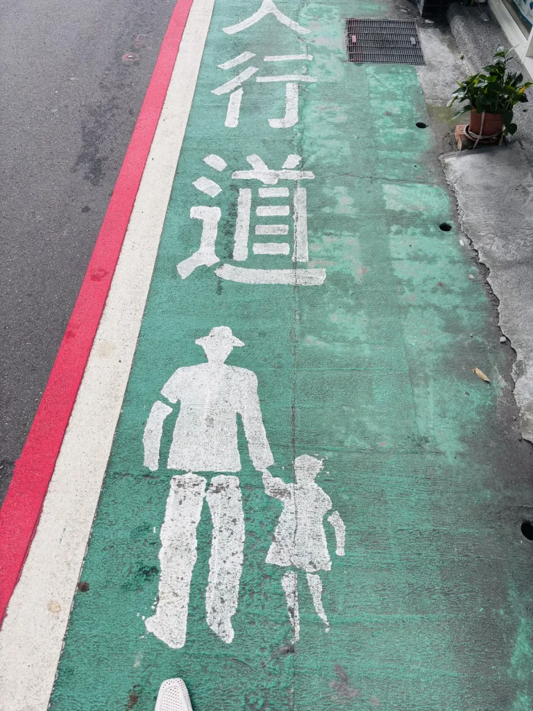 Green pedestrian crosswalk sign painted on a Taipei sidewalk
