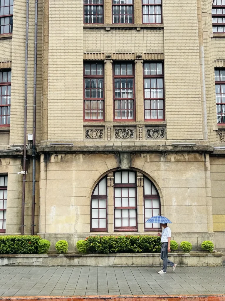Man with an umbrella walking past historic Taipei beimen post office
